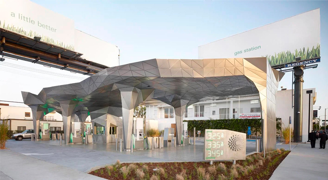 Helios House gas station front-view with a large steel, geometric covering over six silver gas pumps.