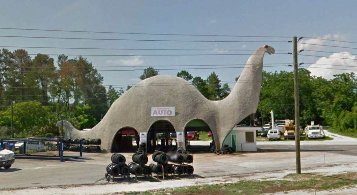 Large grey-colored brachiosaurus with a sign on it that reads 'Harold's Auto Center'.