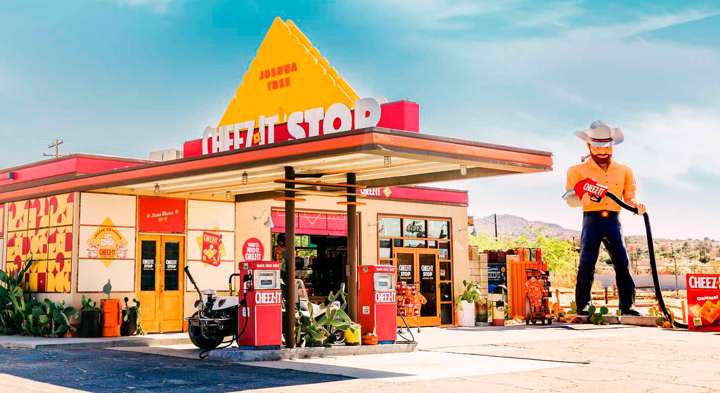 Gas station with Cheez-its snack themed pumps, signage, and a large statue of a man in a cowboy hat holding a Cheez-its gas pump.