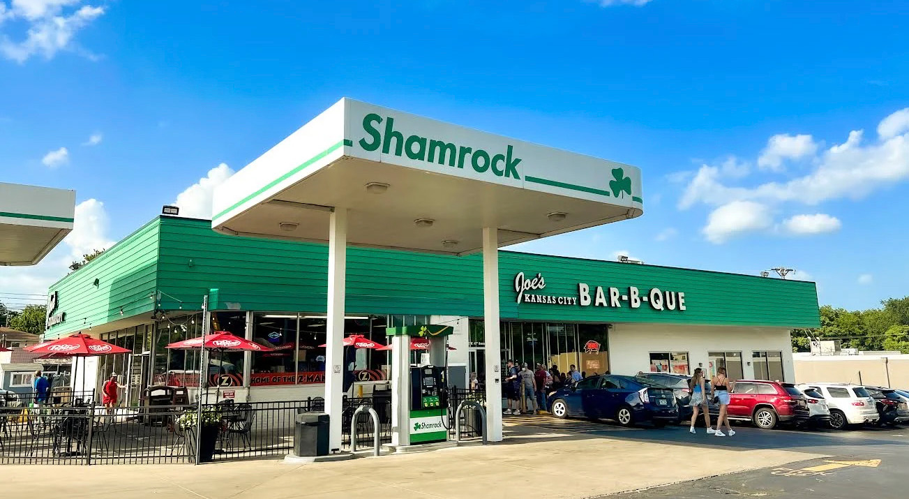 Green gas station that reads 'Shamrock' on the side, infront of a longer buiding that reads 'Joe's Kansas City Bar-B-Que'.